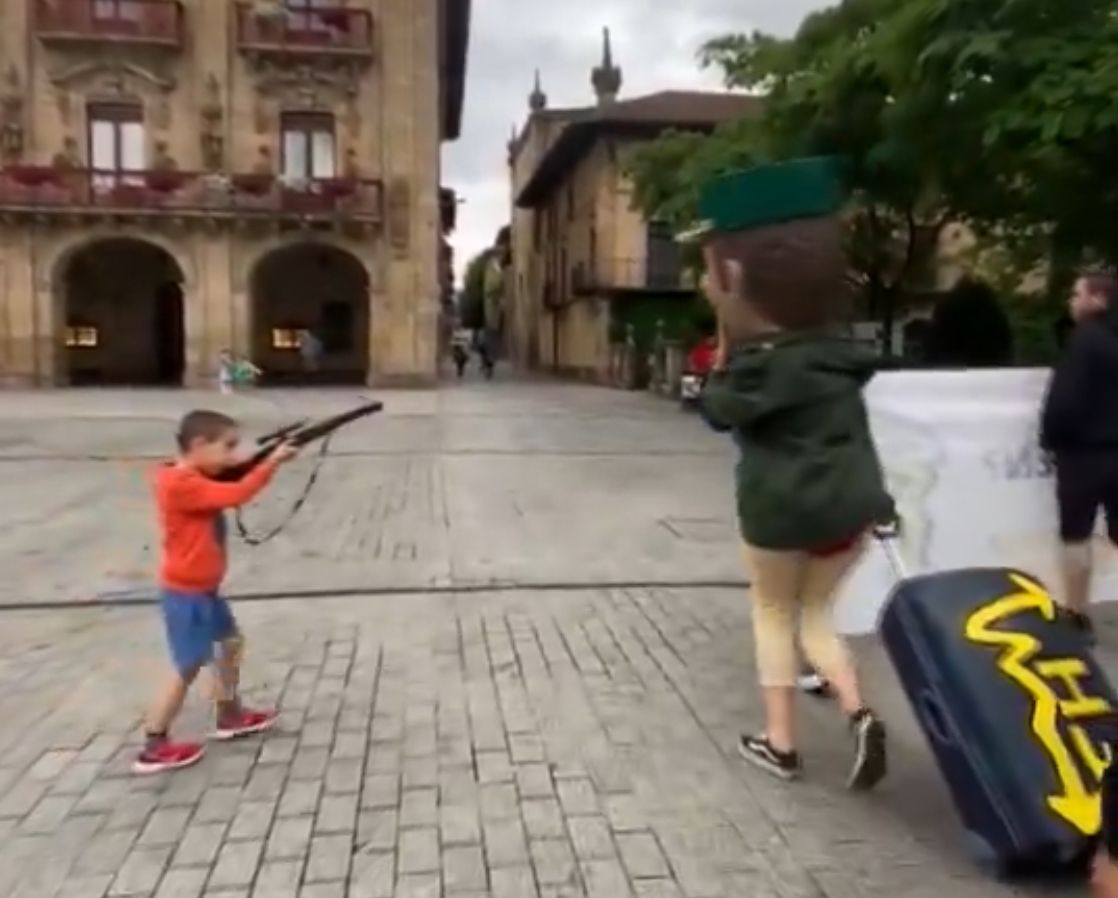 niño apuntando con un rifle de juguete a una persona disfrazada grotescamente de guardia civil 