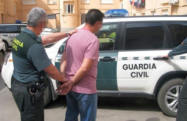 Un guardia civil conduce a un detenido al vehículo oficial..