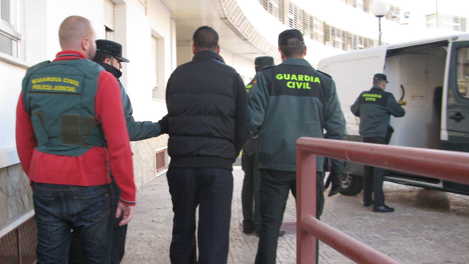 Un detenido es conducido hacia el furgón por parte de varios agentes.