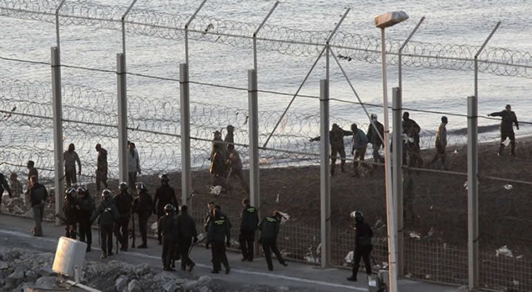 Guardias civiles e inmigrantes en la valla fronteriza del Tarajal, en Ceuta