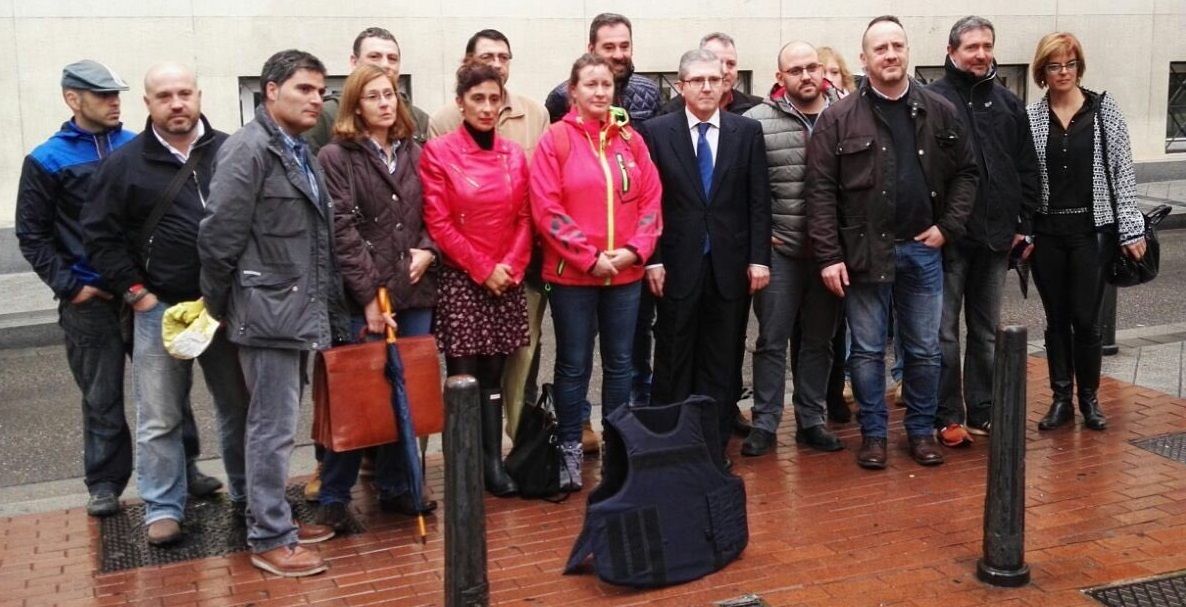 Las guardias civiles Pilar Villacorta y Alicia Sánchez, ambas de rojo, posan a las puertas del tribunal militar de Valladolid con representantes de AUGC frente a un chaleco antibalas.
