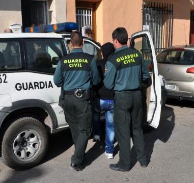 Dos guardias civiles introducen a un detenido en un vehículo oficial