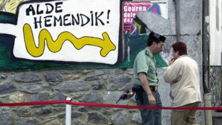 Un guardia civil camina ante una pintada que pide la marcha del Cuerpo de Navarra y el País Vasco.